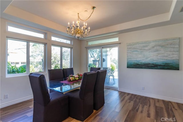 dining area featuring an inviting chandelier, baseboards, a raised ceiling, and wood finished floors