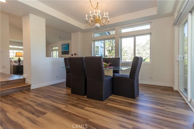 dining room with dark wood-type flooring, a tray ceiling, and a notable chandelier