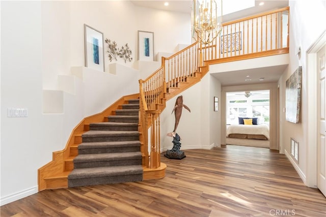 staircase featuring a towering ceiling, baseboards, and wood finished floors