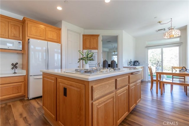 kitchen featuring dark wood-style flooring, light countertops, visible vents, a kitchen island, and white appliances