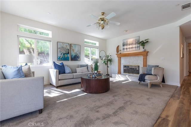 living room with a tile fireplace, wood finished floors, visible vents, baseboards, and a ceiling fan