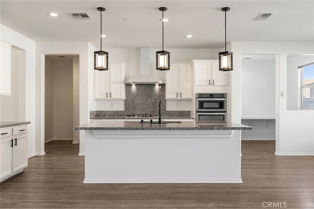 kitchen with wall chimney exhaust hood, dark wood finished floors, visible vents, and white cabinetry