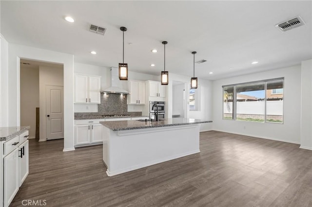 kitchen with backsplash, visible vents, wall chimney range hood, and an island with sink