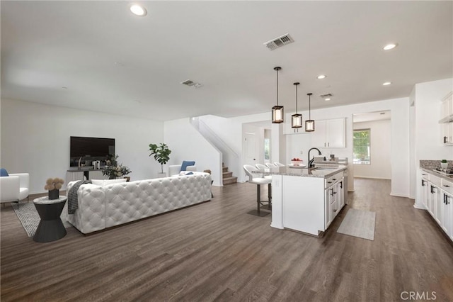 kitchen with a breakfast bar, dark wood-style flooring, visible vents, open floor plan, and white cabinets