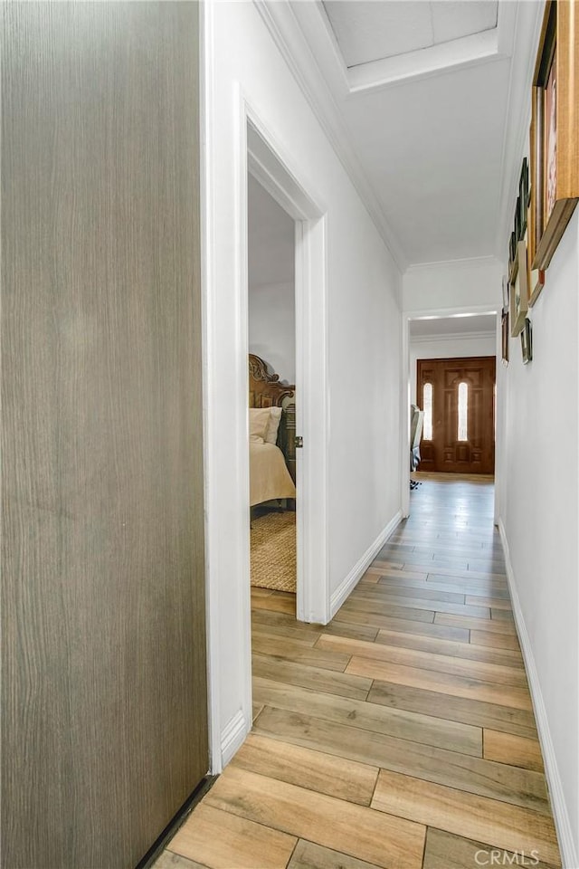 hallway featuring attic access, baseboards, and light wood-style floors