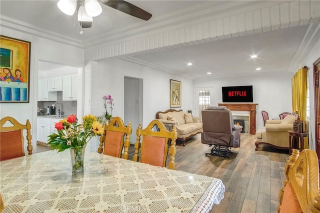 dining room featuring recessed lighting, a ceiling fan, wood finished floors, ornamental molding, and a lit fireplace
