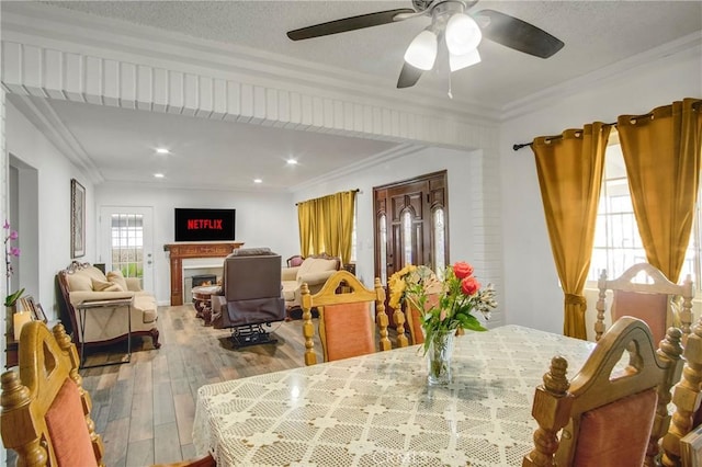 dining space featuring a ceiling fan, crown molding, hardwood / wood-style flooring, a lit fireplace, and recessed lighting