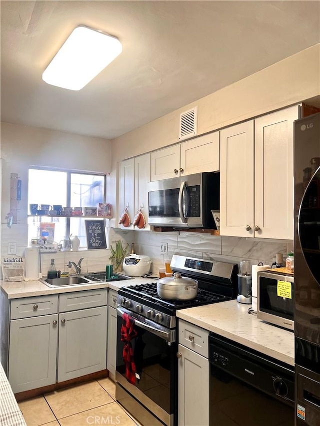 kitchen featuring light tile patterned floors, visible vents, a sink, decorative backsplash, and stainless steel appliances