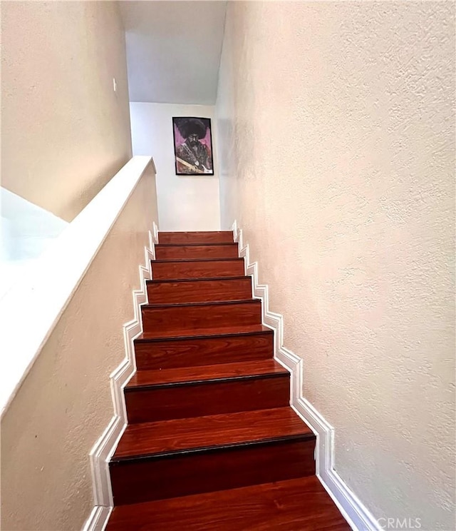 staircase featuring wood finished floors and a textured wall