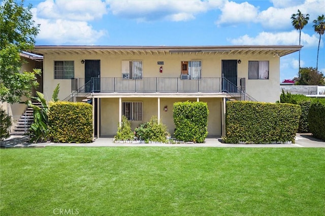 view of front of house featuring stairs, a front lawn, and stucco siding