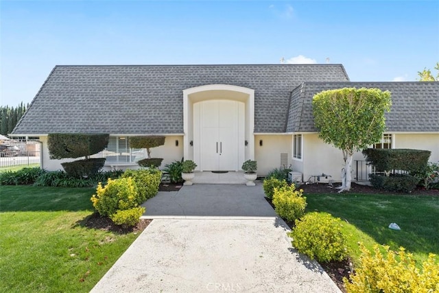 view of front of property with a shingled roof, mansard roof, a front lawn, and stucco siding