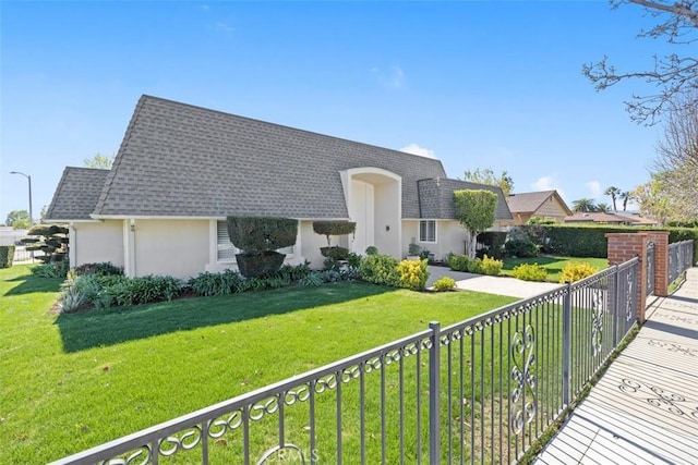 view of front of property with a front yard, roof with shingles, fence, and stucco siding