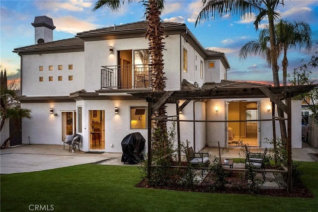 back of property at dusk with a yard, a patio, a balcony, and stucco siding