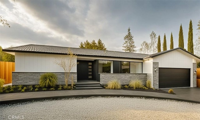 view of front of property with fence, a garage, stone siding, driveway, and a tiled roof