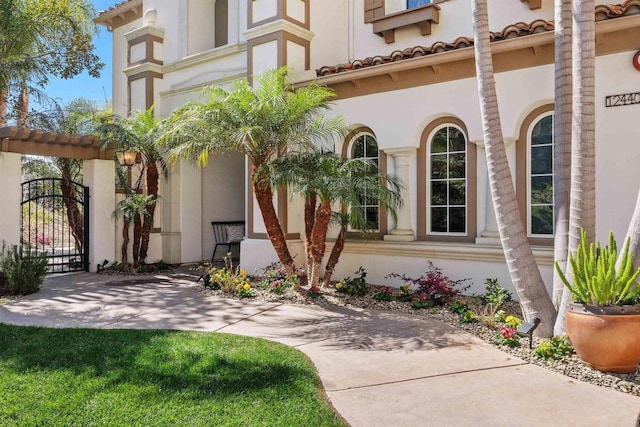 view of exterior entry with a tiled roof, a gate, and stucco siding