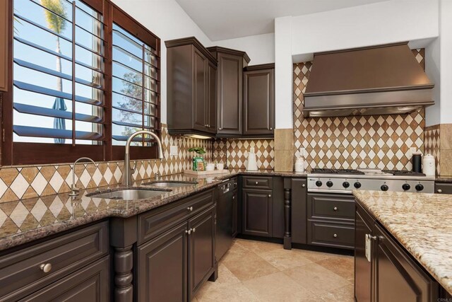 kitchen with stone countertops, premium range hood, a sink, backsplash, and stainless steel gas stovetop