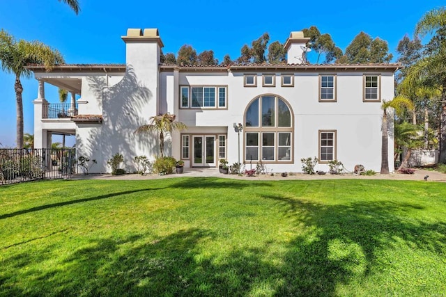 back of property featuring french doors, a chimney, stucco siding, a lawn, and a balcony