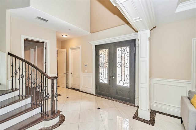 foyer featuring visible vents, wainscoting, stairway, french doors, and a decorative wall