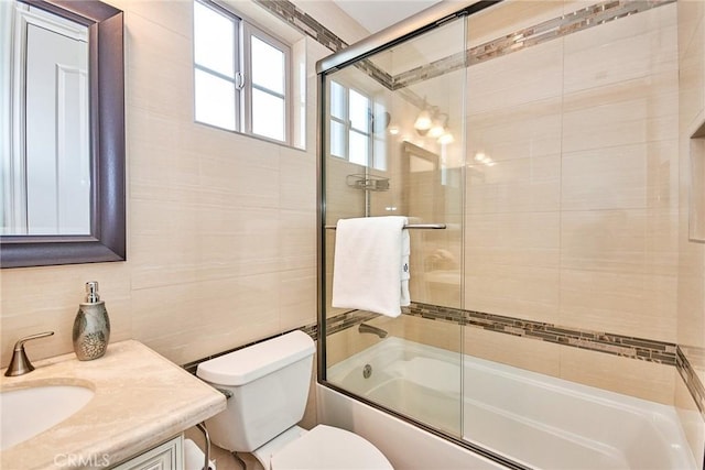 bathroom featuring toilet, combined bath / shower with glass door, vanity, and tile walls