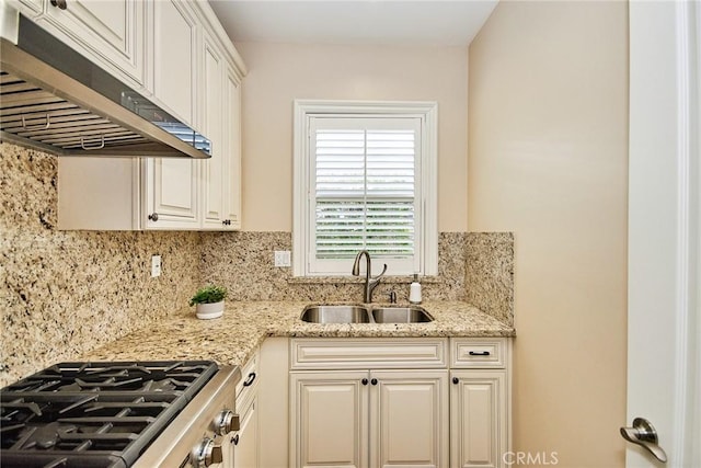 kitchen with tasteful backsplash, light stone countertops, stovetop, under cabinet range hood, and a sink