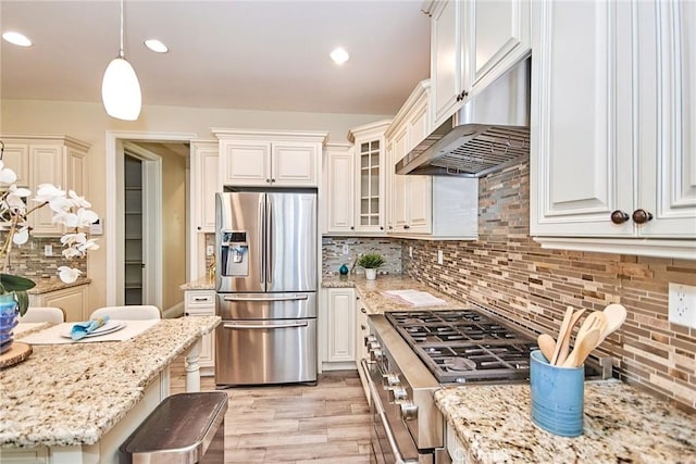 kitchen featuring light wood finished floors, decorative light fixtures, stainless steel appliances, under cabinet range hood, and backsplash