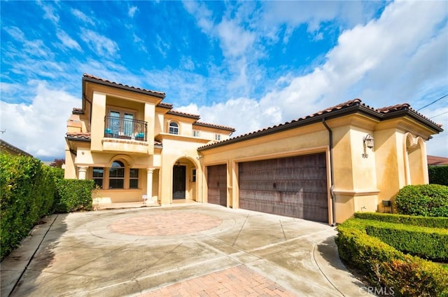 mediterranean / spanish house featuring a garage, concrete driveway, a balcony, and stucco siding