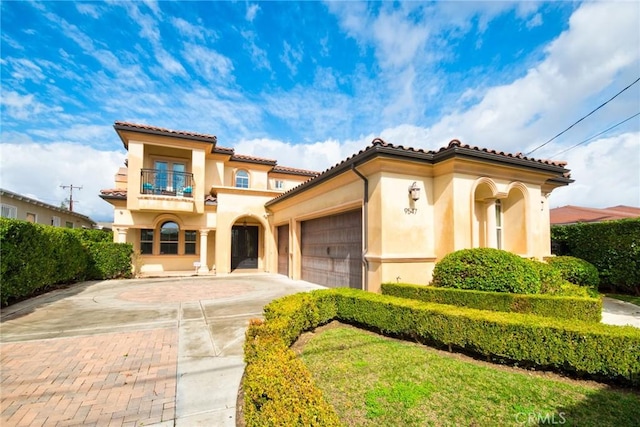 mediterranean / spanish house featuring a garage, driveway, a balcony, and stucco siding