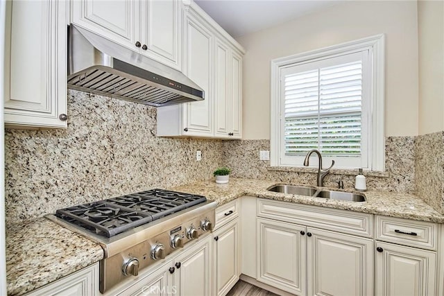 kitchen with stainless steel gas cooktop, a sink, under cabinet range hood, and backsplash