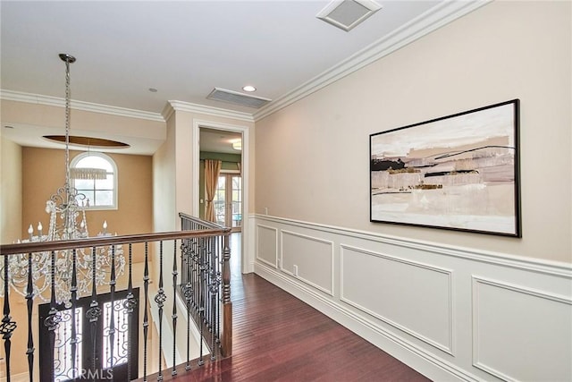 hall with a decorative wall, an upstairs landing, wainscoting, dark wood-style floors, and crown molding