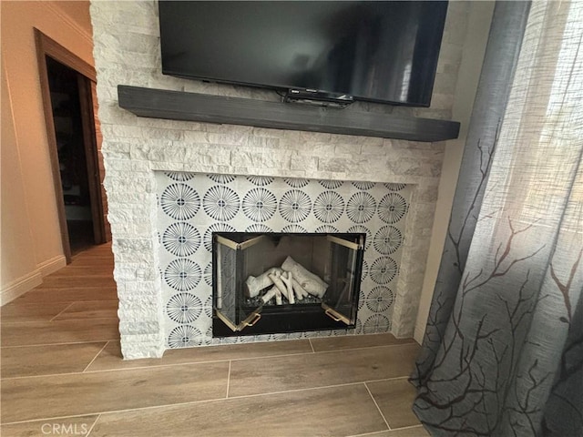 room details featuring wood finish floors, a stone fireplace, and baseboards