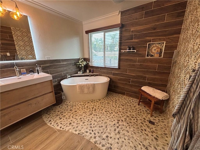 bathroom with wood finished floors, vanity, tile walls, ornamental molding, and a soaking tub