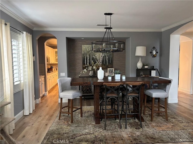 dining room with arched walkways, ornamental molding, wood finished floors, and visible vents