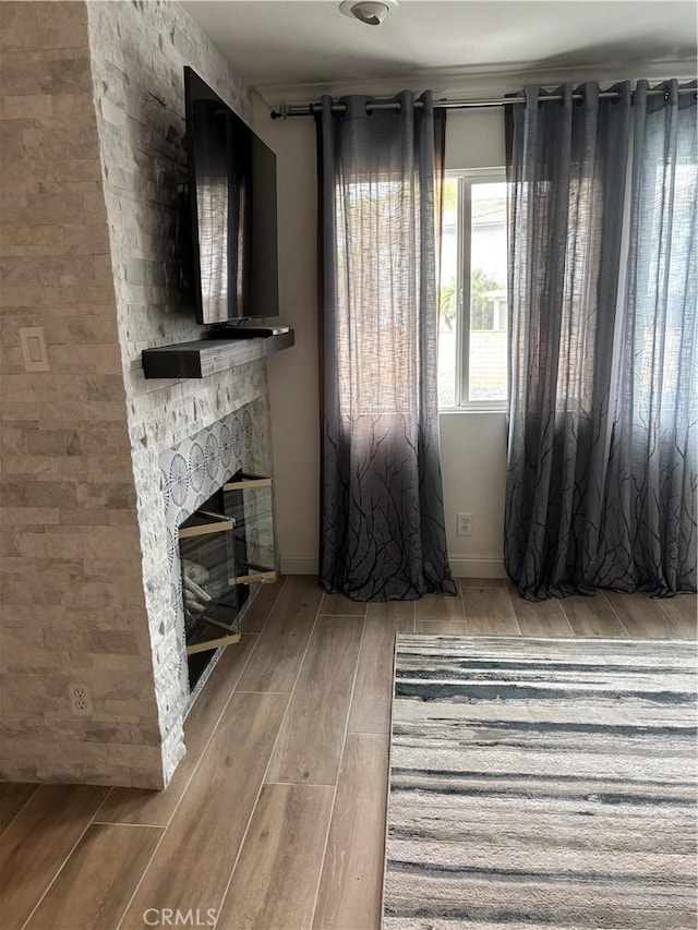 unfurnished living room featuring wood tiled floor, baseboards, and a stone fireplace