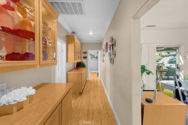 corridor with ornamental molding, baseboards, light wood-type flooring, and visible vents