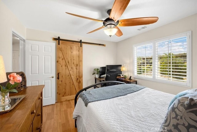 bedroom featuring light wood-type flooring, ceiling fan, visible vents, and a barn door