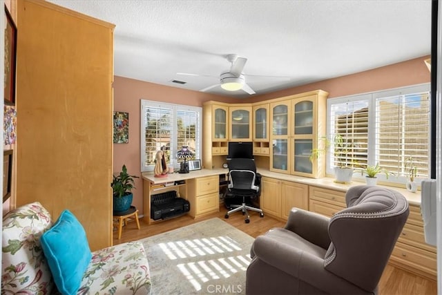 office area featuring ceiling fan, a textured ceiling, visible vents, light wood-type flooring, and built in study area