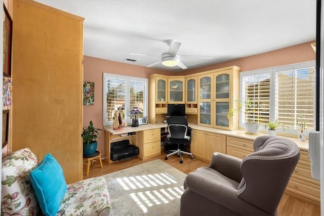office featuring built in study area, light wood-type flooring, a ceiling fan, and visible vents