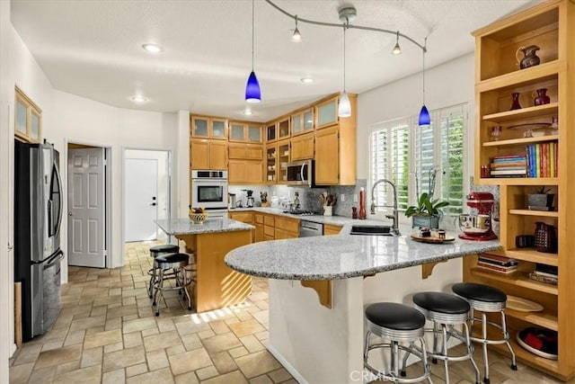 kitchen with light stone counters, a sink, a kitchen bar, a peninsula, and appliances with stainless steel finishes