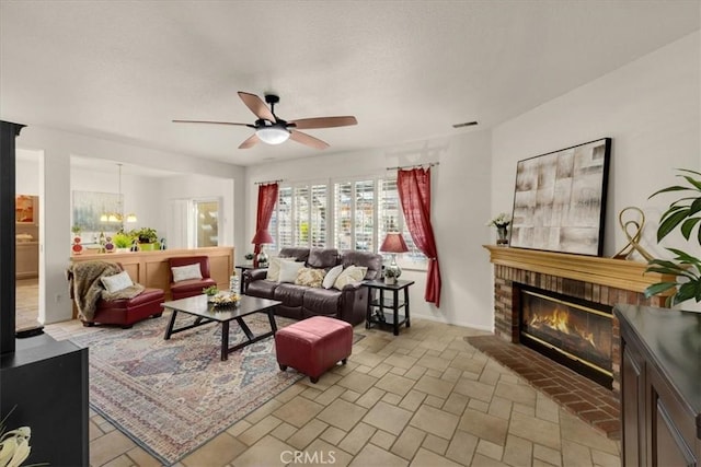 living area with ceiling fan with notable chandelier, stone finish floor, a fireplace, and visible vents