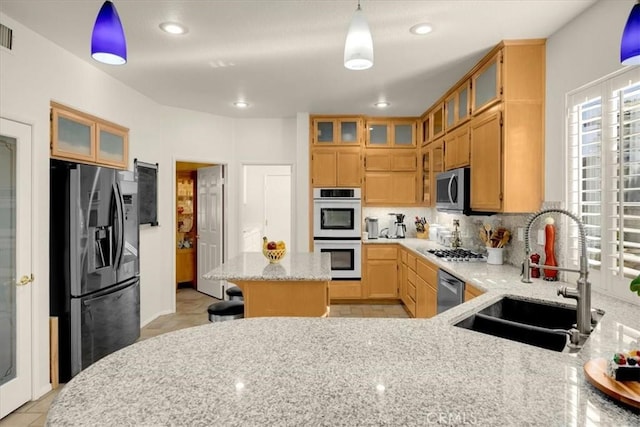 kitchen featuring light tile patterned flooring, stainless steel appliances, a sink, backsplash, and light stone countertops