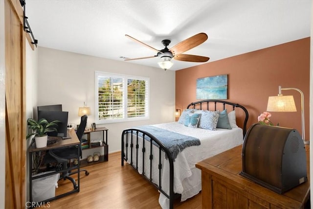 bedroom with ceiling fan, visible vents, a barn door, and wood finished floors