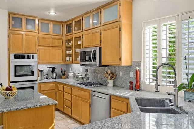 kitchen with appliances with stainless steel finishes, a sink, backsplash, and light stone counters