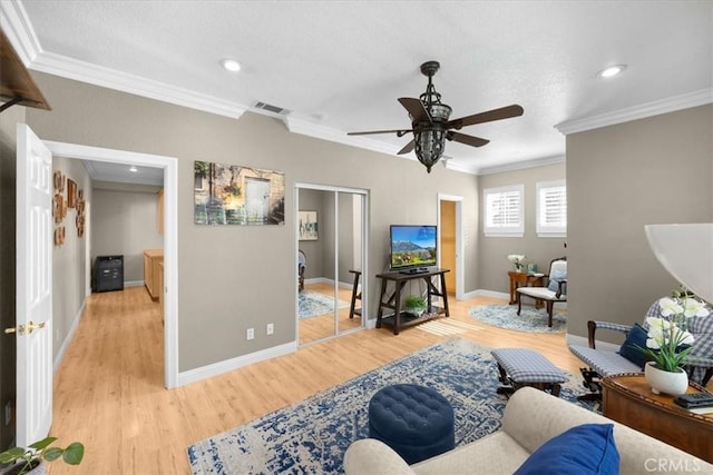 living room with light wood finished floors, visible vents, ornamental molding, ceiling fan, and baseboards