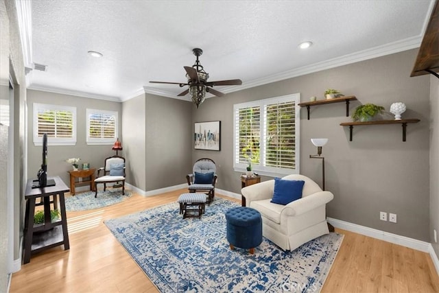 living area featuring a textured ceiling, visible vents, baseboards, light wood finished floors, and crown molding