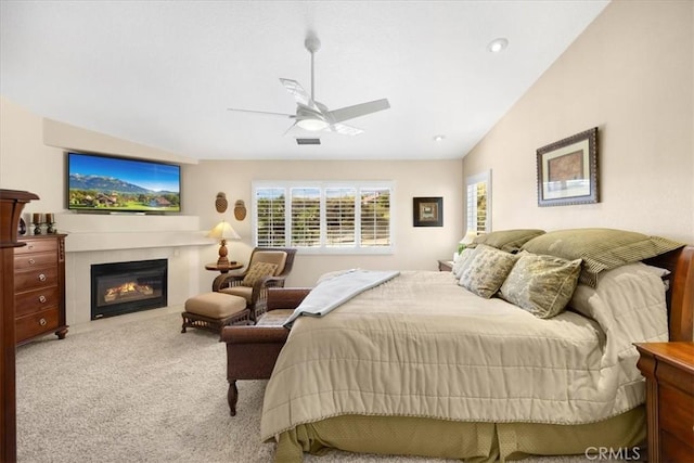 carpeted bedroom featuring ceiling fan, vaulted ceiling, a glass covered fireplace, and visible vents