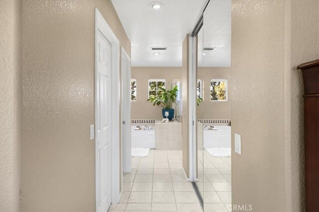 hall with a textured wall, light tile patterned flooring, and visible vents