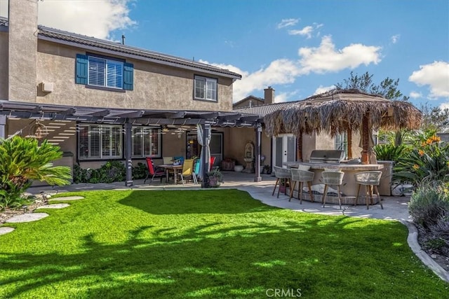 rear view of house with stucco siding, a pergola, area for grilling, outdoor dry bar, and a yard