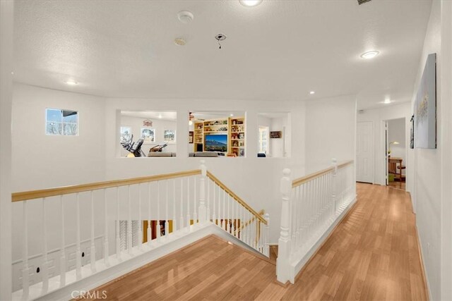 hall with light wood-style floors, recessed lighting, a textured ceiling, and an upstairs landing