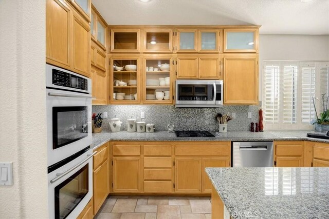 kitchen with stainless steel appliances, stone finish floor, glass insert cabinets, and tasteful backsplash