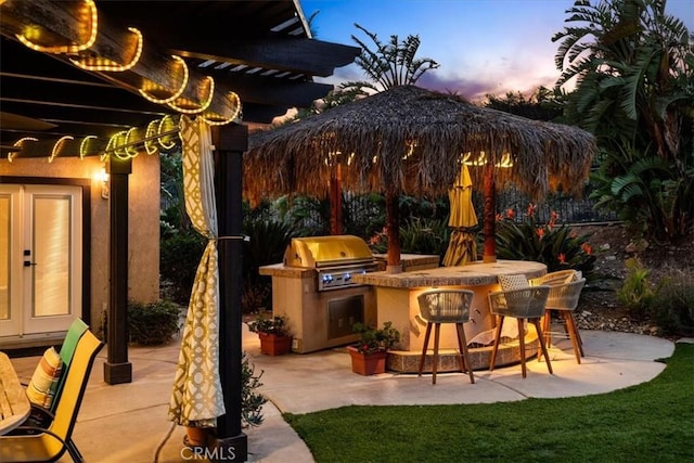 patio terrace at dusk featuring exterior kitchen, a bar, and a grill